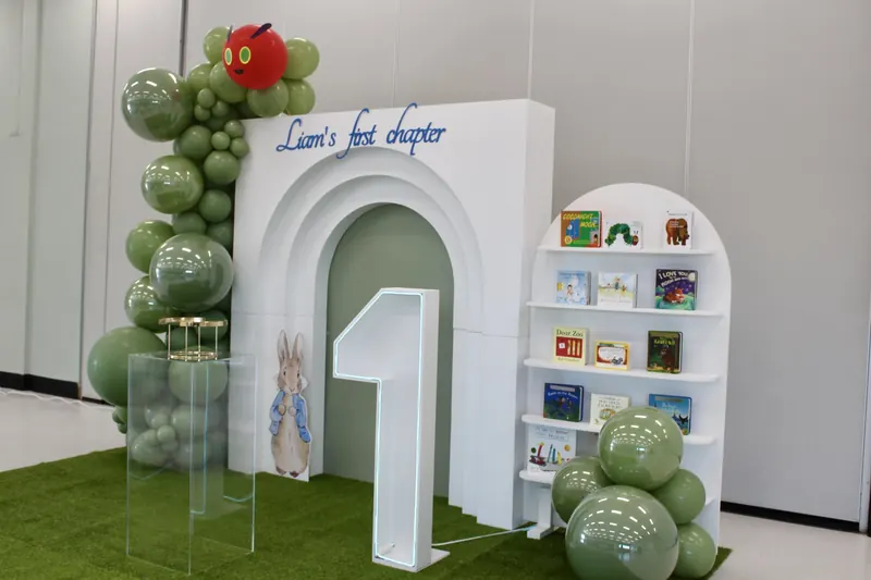 The same hall styled with balloons, an arch, books and a grass stage