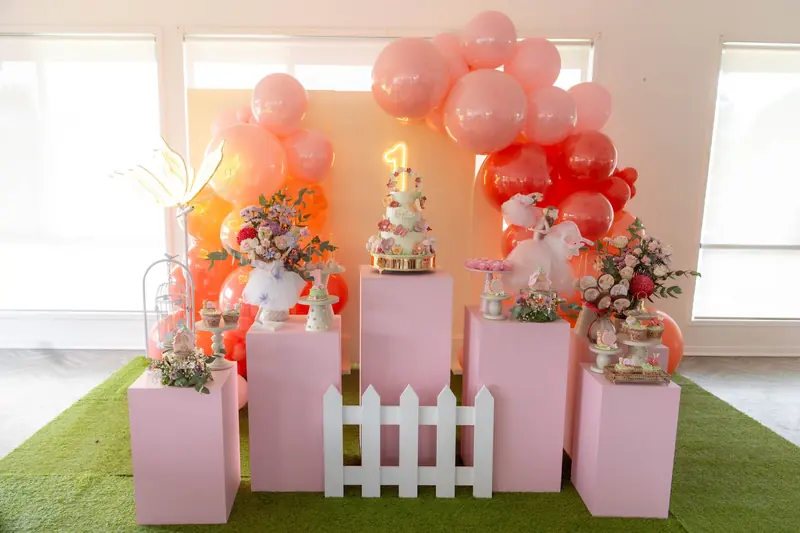 Sophie First Birthday: Coral and blush balloons, pink plinths, a white picket fence and fairy details.