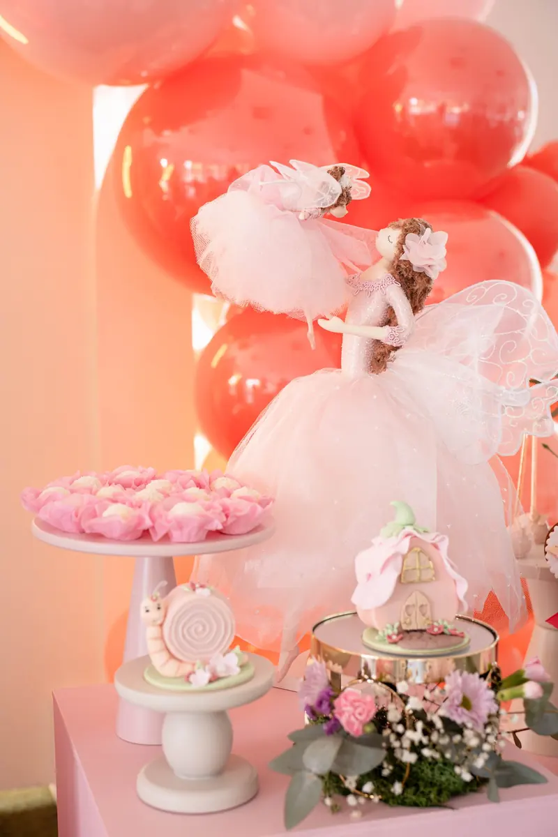 Fairy figurine in a tulle dress beside a dessert stand and pastel florals